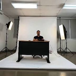 Empty portrait studio with a white backdrop and two softbox lights, photographer seated at a desk