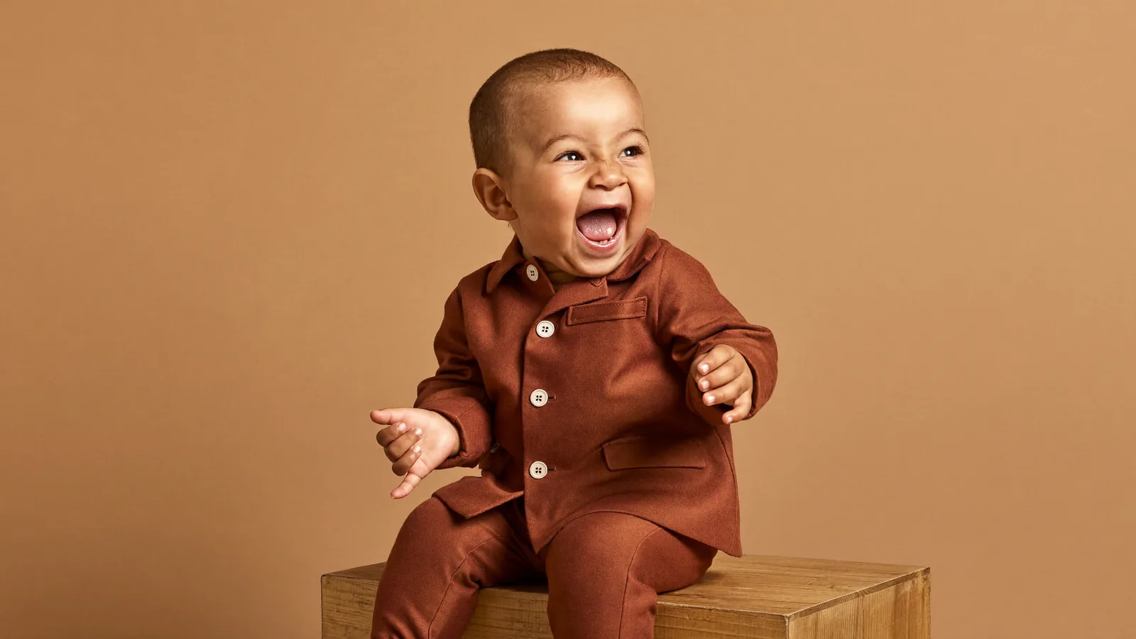 A giggling toddler in a tiny suit during a timeless children's portrait session